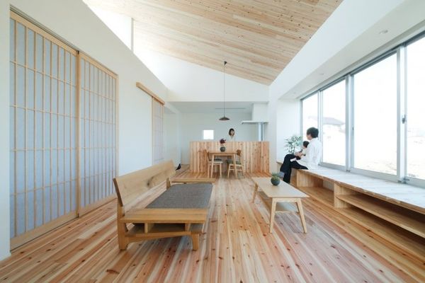 Una habitación iluminada con piso de madera y muebles de madera. En la izquierda al lado de un ventanal un hombre con un niño en su regazo 