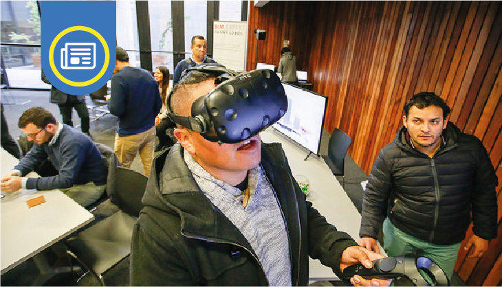 Un hombre con unas gafas de realidad virtual y un control en la mano. De fondo varias personas caminando